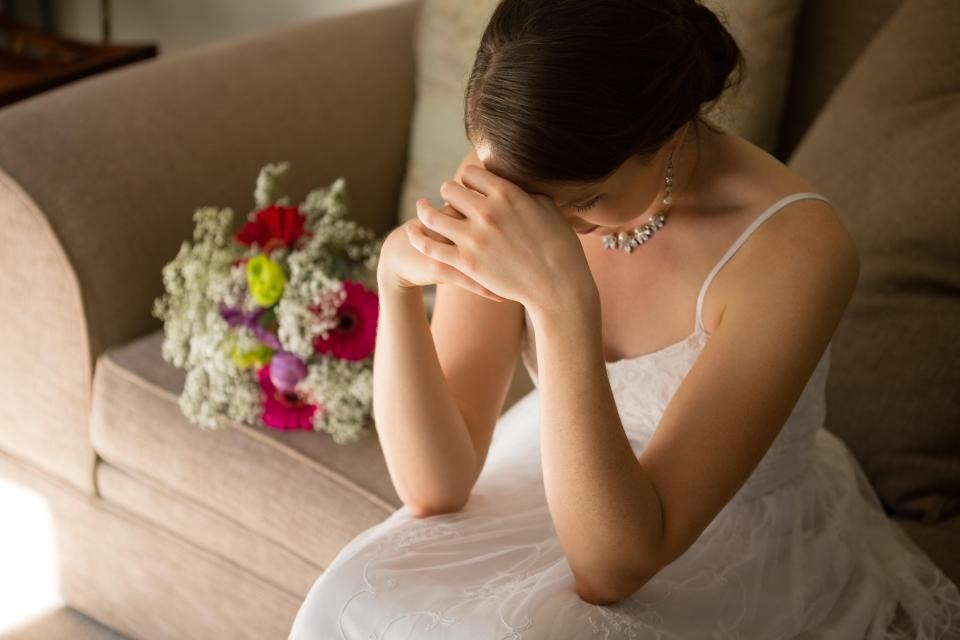 Upset bride sitting by a bouquet on a sofa.