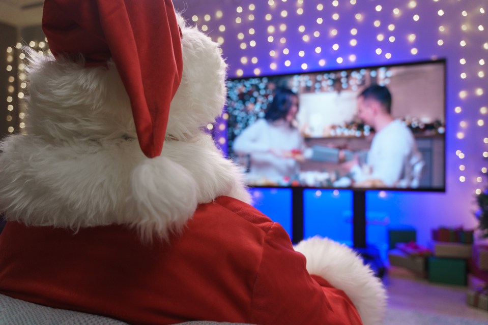 Santa Claus watching TV from behind, distracted from leaving gifts.
