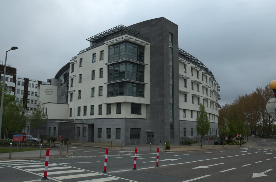 Cork University Hospital building with an adjacent road, crosswalk, and trees.