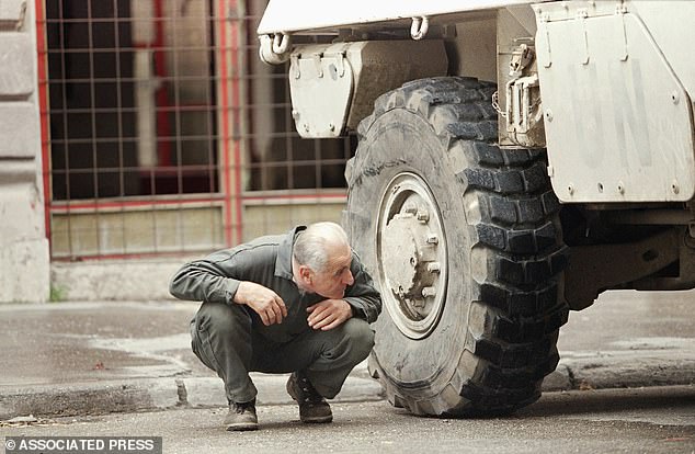 Seeking shelter behind a United Nations APC, a Sarajevan man pinned down by sniper fire, peers from behind the wheel in Sarajevo, 1995