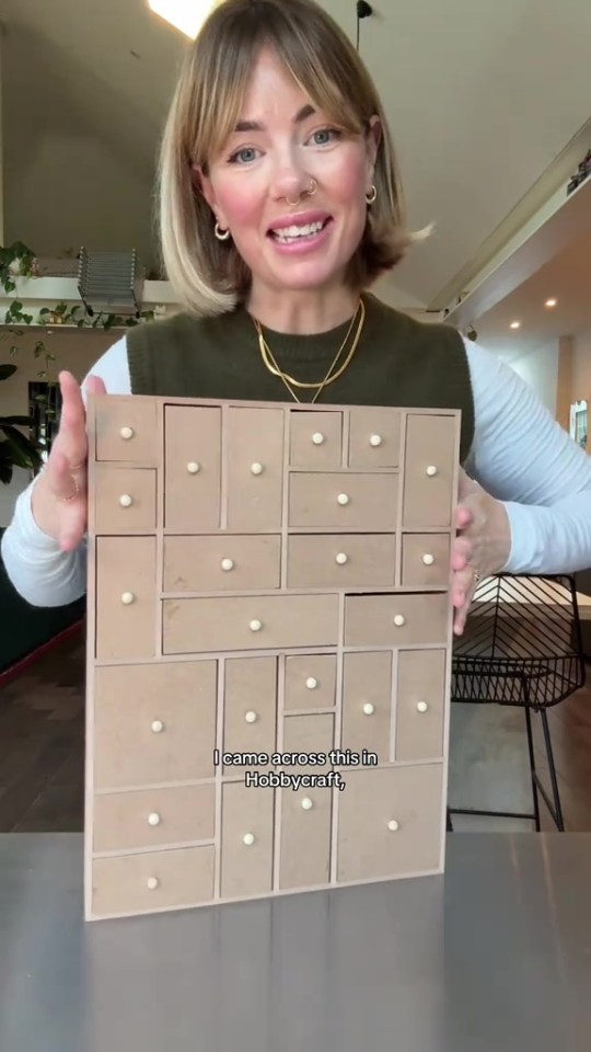 A woman holding a wooden Advent calendar with multiple small drawers.