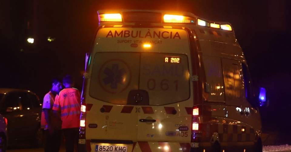 An ambulance with flashing lights and two emergency workers at night.