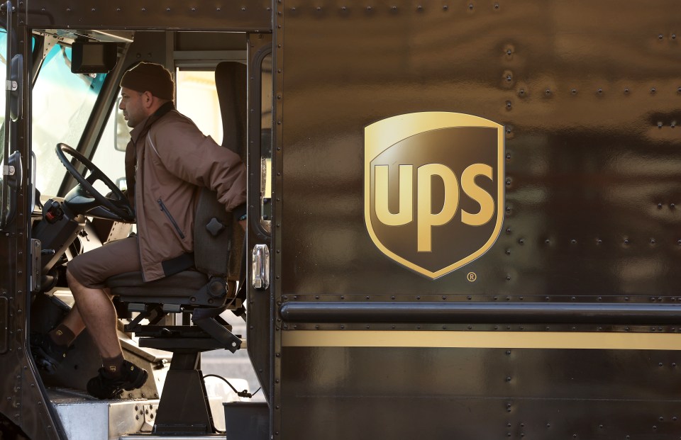A UPS driver sitting in the cab of his delivery truck, with the UPS logo visible on the side.