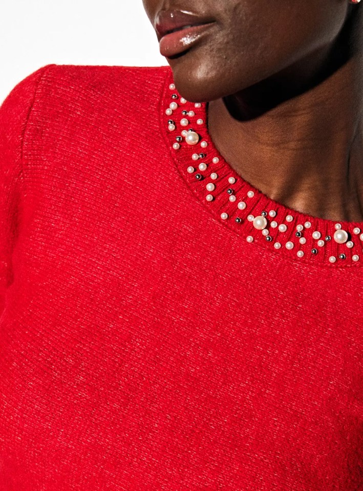 Close-up of a person wearing a red sweater with pearls and silver beads around the neckline.