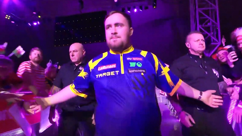 A man in a blue and yellow shirt high-fives people in the crowd as he walks past them.