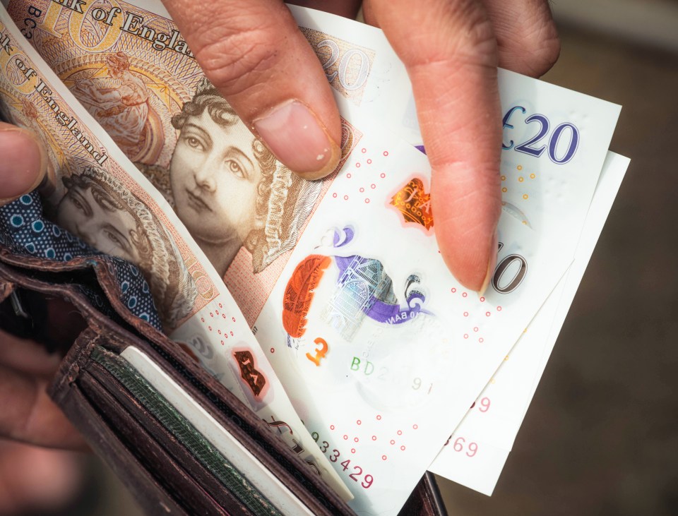A person holding a wallet containing British ten and twenty pound notes.