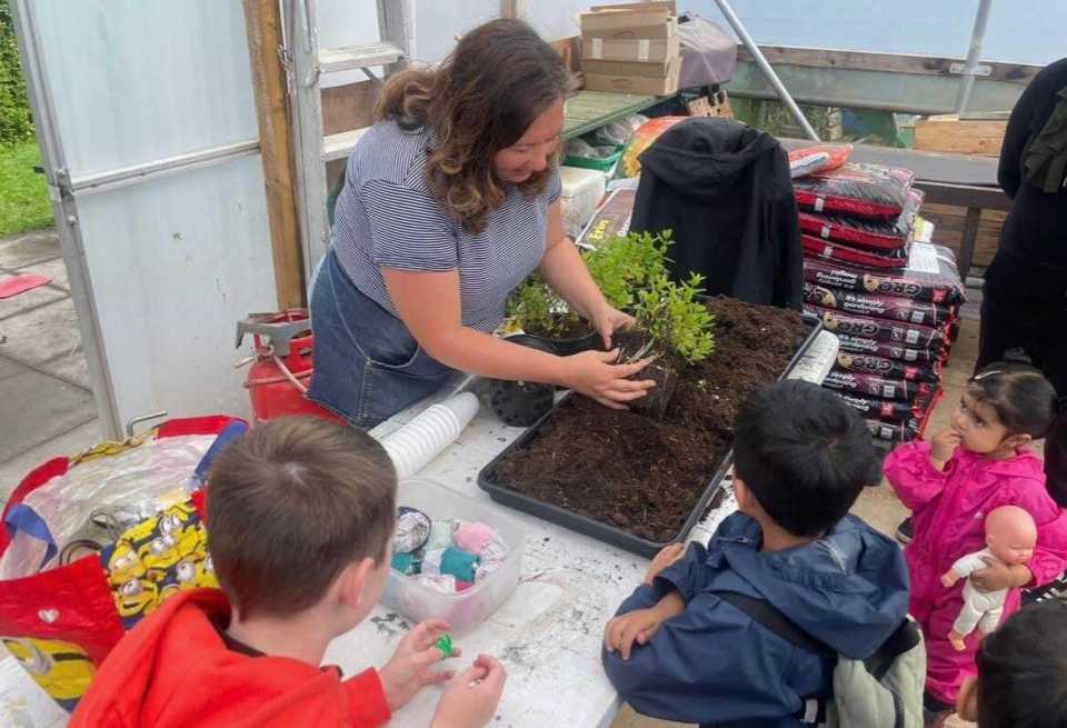 Woman in striped shirt and denim apron teaching children how to pot a plant.