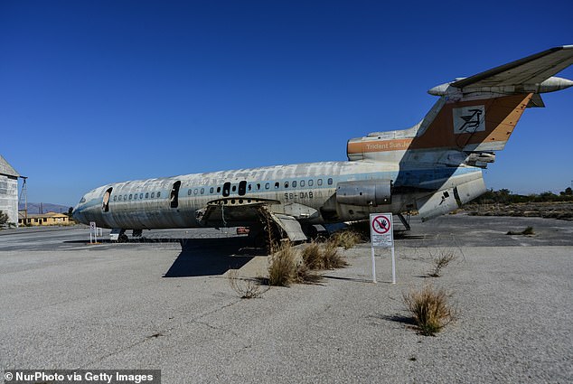 Out on the runway, the shell of a solitary passenger jet sits on the tarmac, riddled with bullet holes