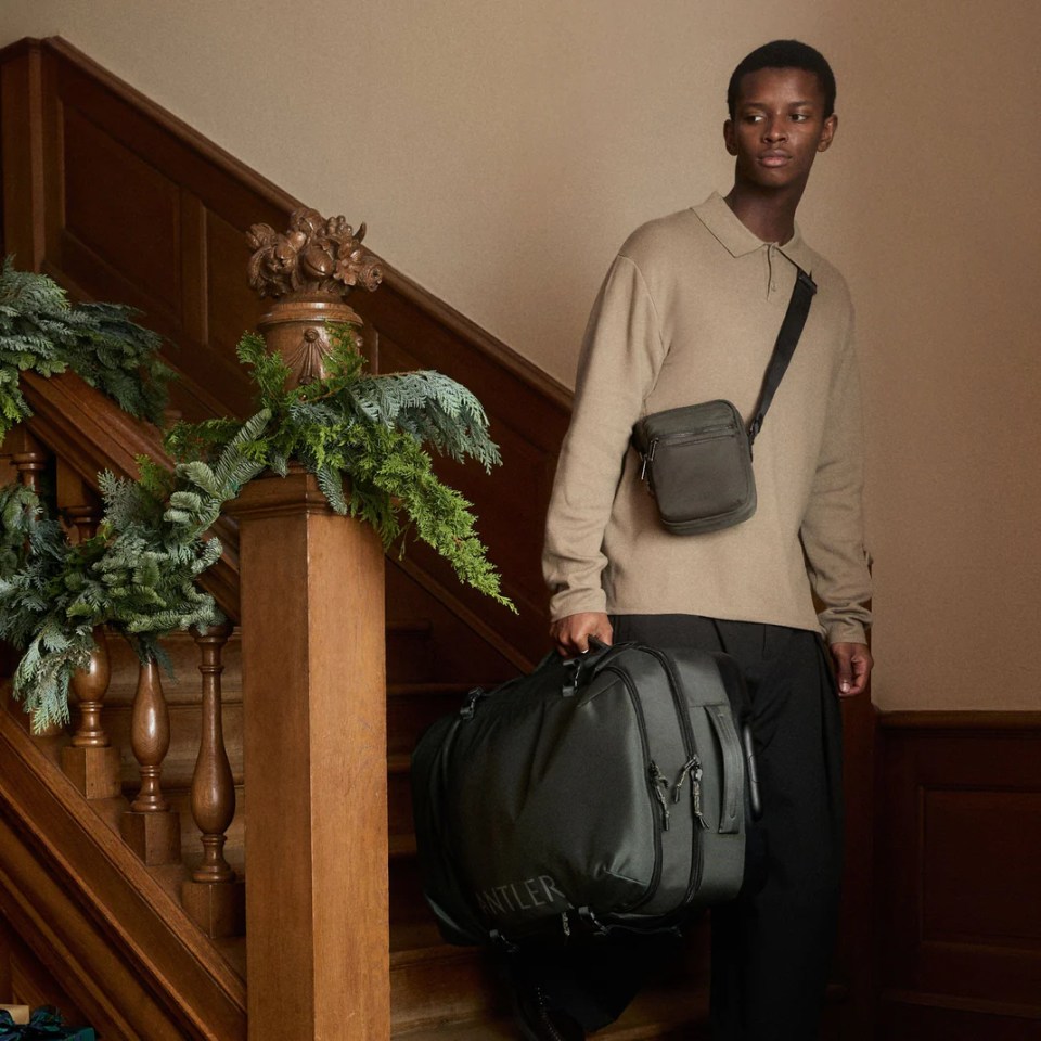 Man carrying a black duffel bag and shoulder bag down a wooden staircase.