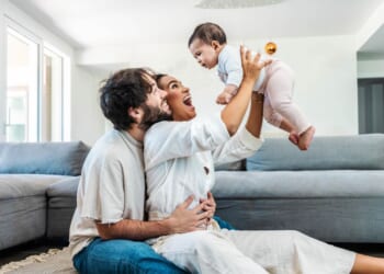 A husband and wife play with their daughter at home.