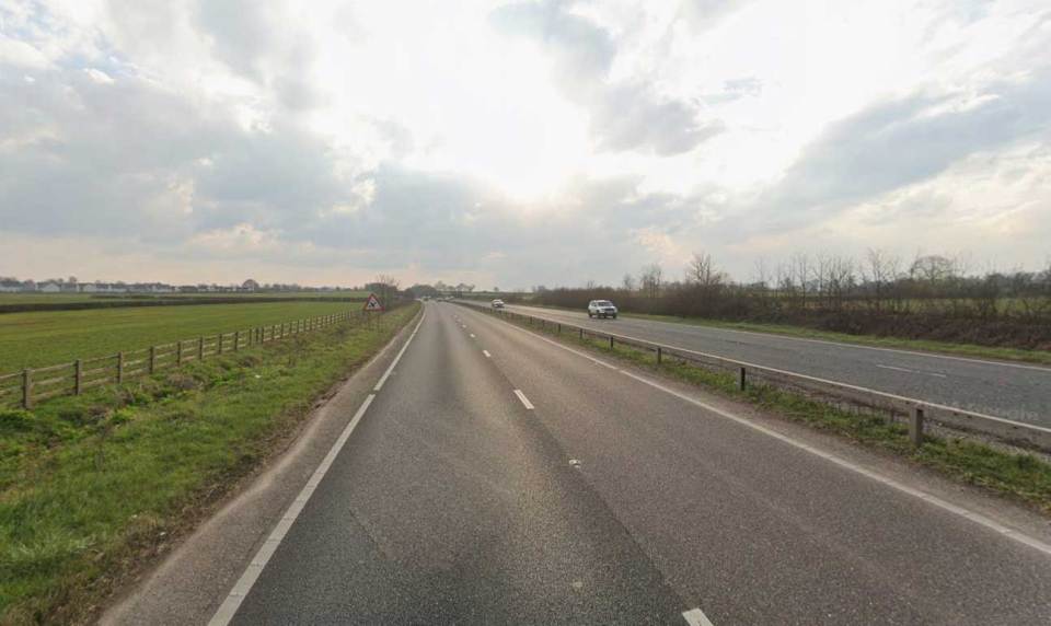 A two-lane highway with a grassy median and fields on either side.