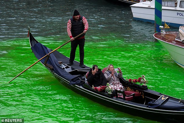 People enjoy a gondola ride on the Grand Canal, where the canal's water has been dyed green in a protest organised by the 'Extinction Rebellion' climate activists, in Venice, Italy, November 22, 2025