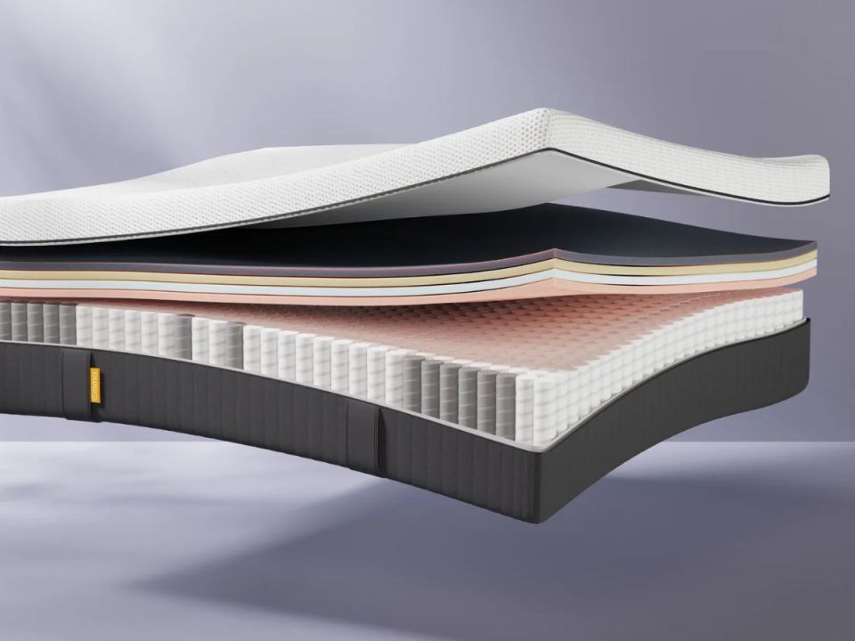 Illustration of a mattress with visible layers, including a top white textured cover, several foam layers in different colors, and a base layer of springs.