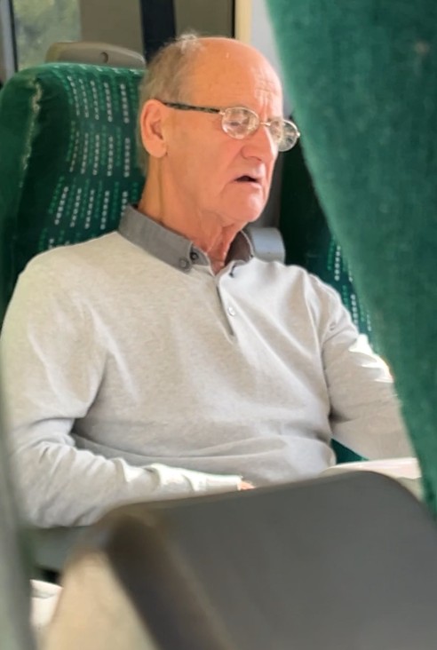 A man with glasses and a light grey polo shirt looks towards the right.