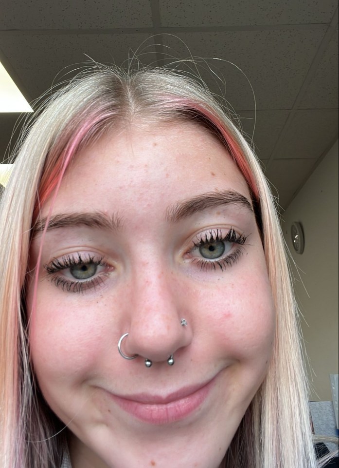 A smiling young woman with blonde and pink-streaked hair, green eyes, and nose piercings.