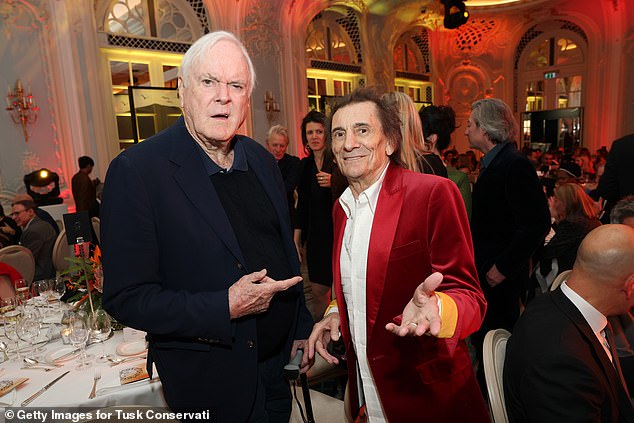 The guitarist turned heads in his very festive ensemble, sporting a red velvet jacket over a button-up shirt and a pair of skinny black trousers covered in glitter (seen with John Cleese)