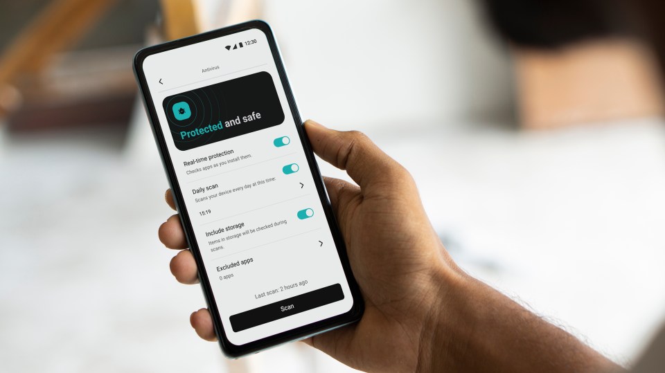 Hand holding a smartphone showing the Antivirus section of Surfshark One, with "Protected and safe" displayed on the screen.