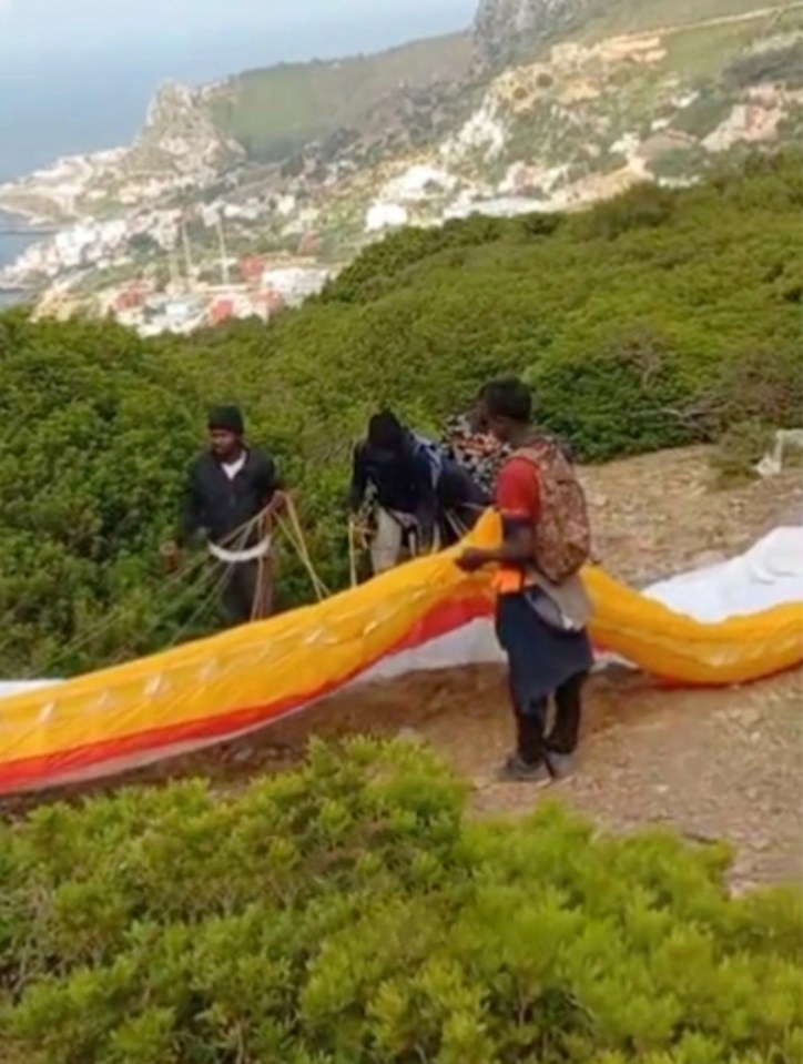 Three men preparing to paraglide over a city by the sea.