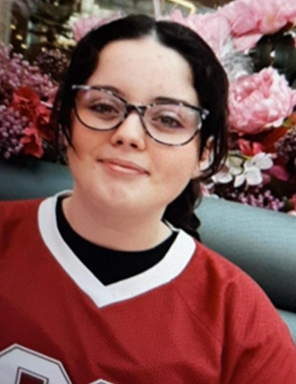 Ava, a 13-year-old girl with dark hair and glasses, wearing a red jersey.