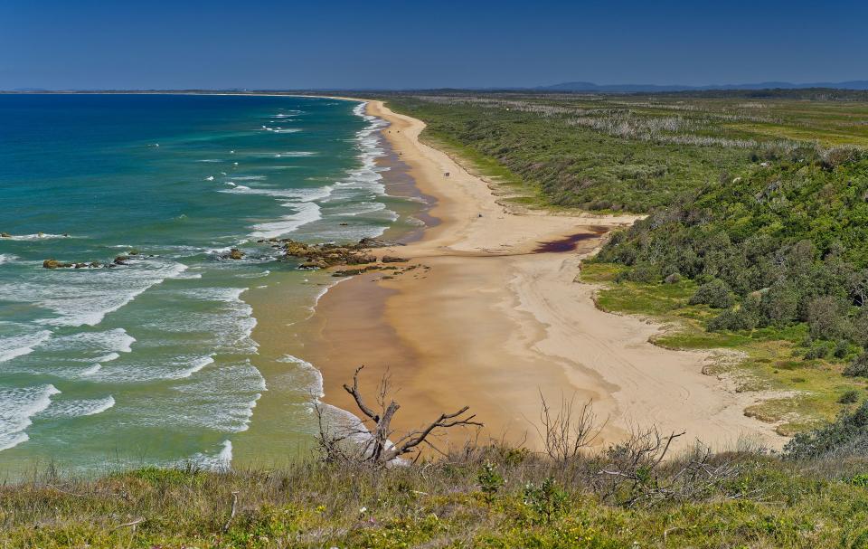 Long sandy beach with breaking waves and coastal heathland at Crowdy Bay, New South Wales, Australia