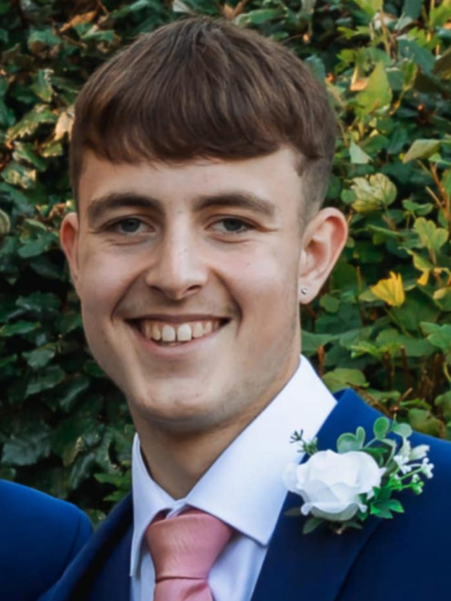 Ethan Powell, a young man smiling and wearing a blue suit with a pink tie and a white boutonnière.