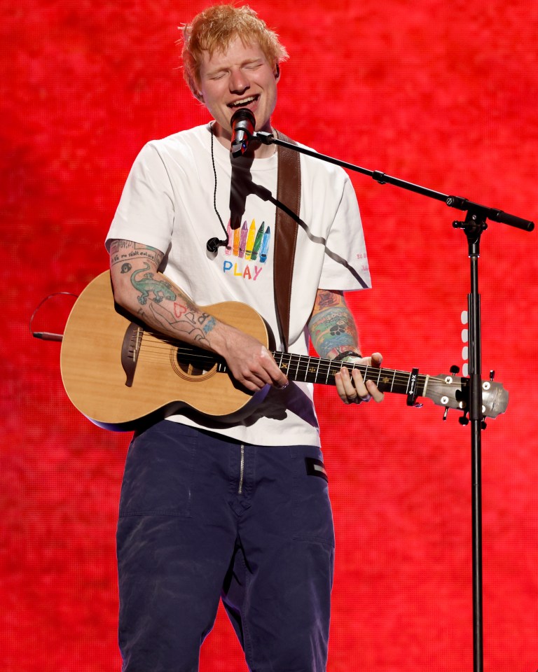 Ed Sheeran performing onstage, singing into a microphone and playing an acoustic guitar.