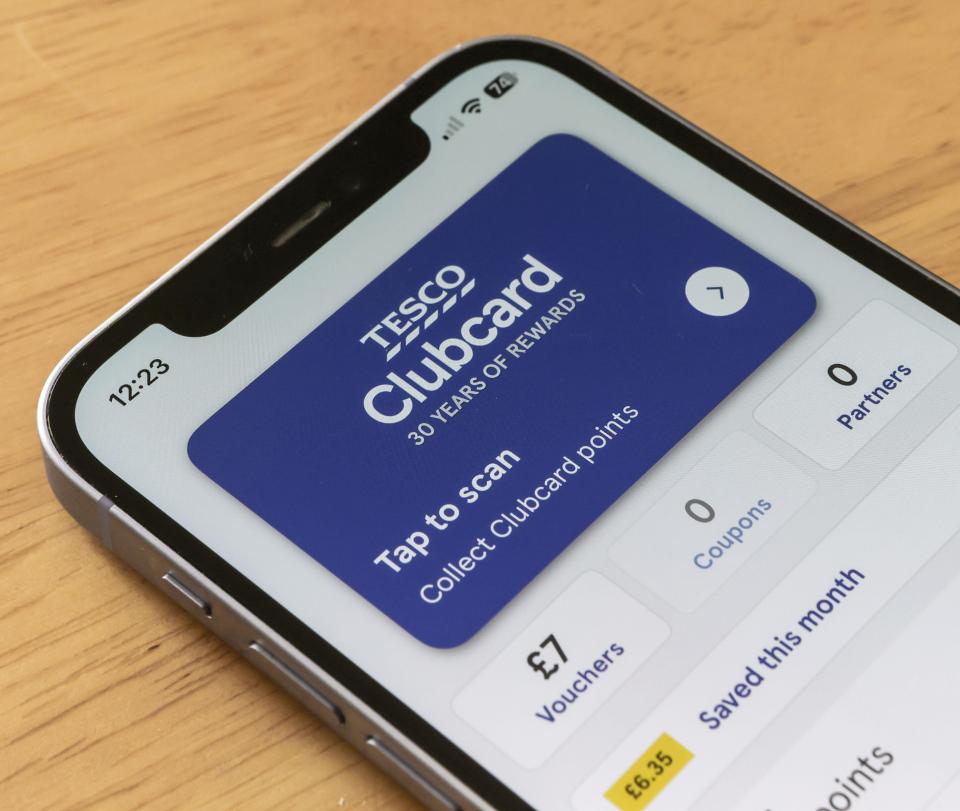 Tesco Clubcard app displayed on an iPhone screen, showing a blue "Tap to scan" card and "£7 Vouchers" and "£6.35 Saved this month".