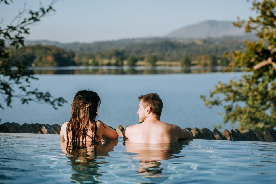 Two people in an outdoor infinity spa pool overlooking Lake Windermere.