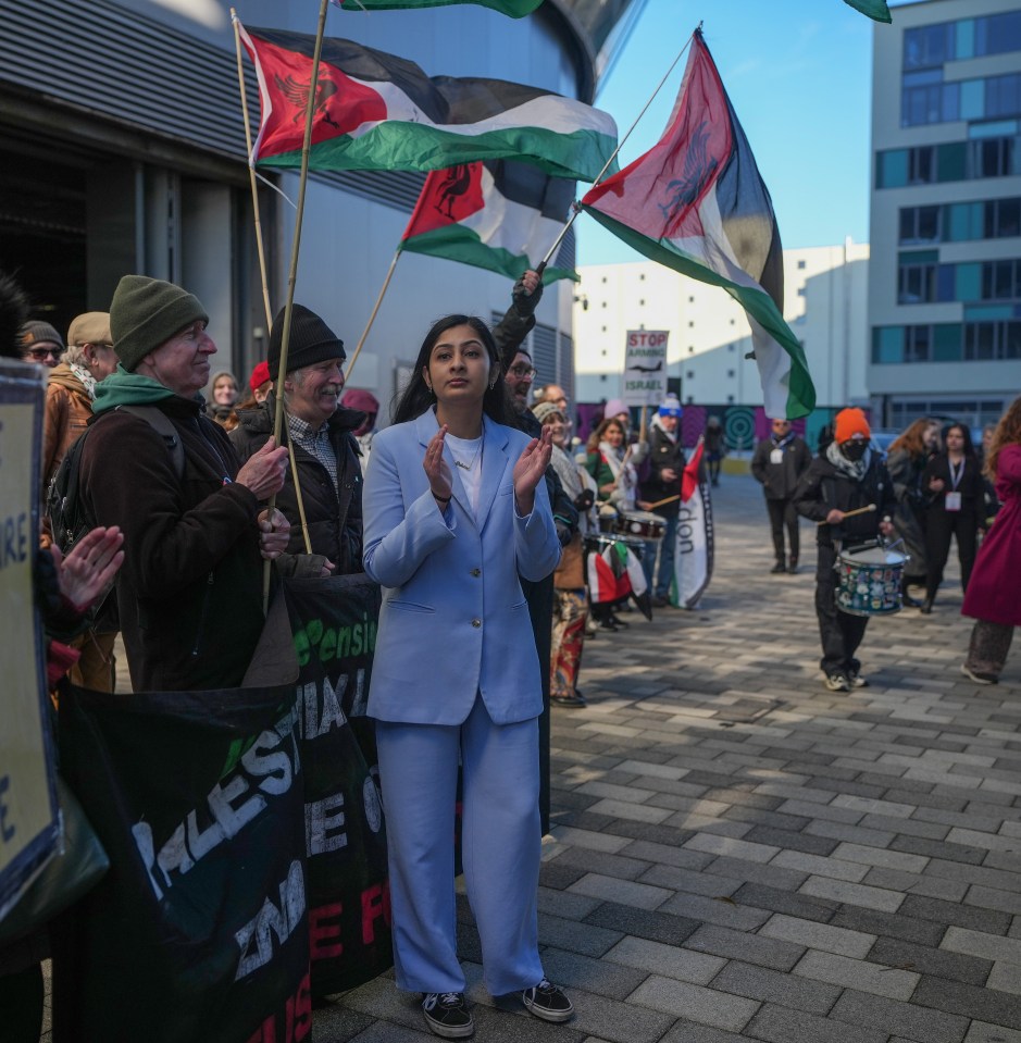 People gathered for a conference with banners, Palestinian flags, and signs that read "The Ceasefire is a lie" and "Stop Arming Israel."