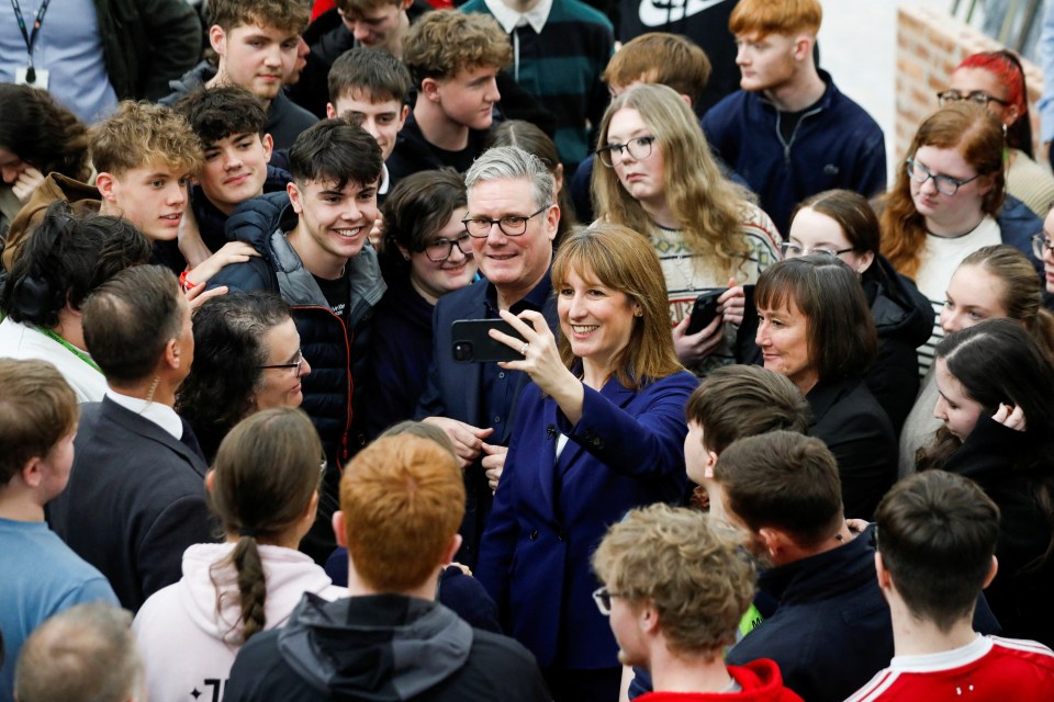 Keir Starmer and a woman in a blue suit smiling while taking a selfie with a group of young people.