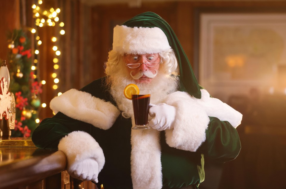 Green Santa holding a mulled wine with an orange slice.