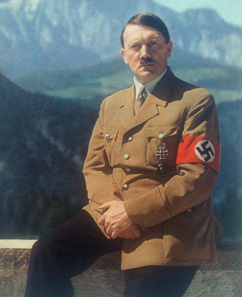 Adolf Hitler in uniform with a swastika armband, sitting outdoors with mountains in the background.
