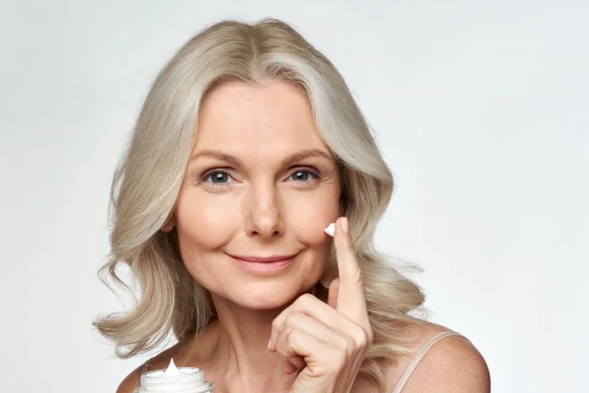 An image collage containing 1 images, Image 1 shows A smiling middle-aged woman applying facial cream to her cheek