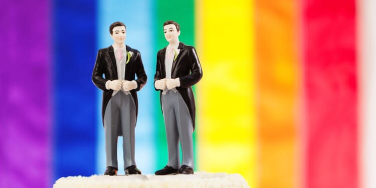 A so-called "gay" marriage wedding cake in front of a pride flag.