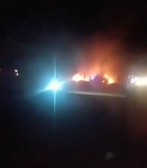 A building on fire at night with a car's bright headlights in the foreground.