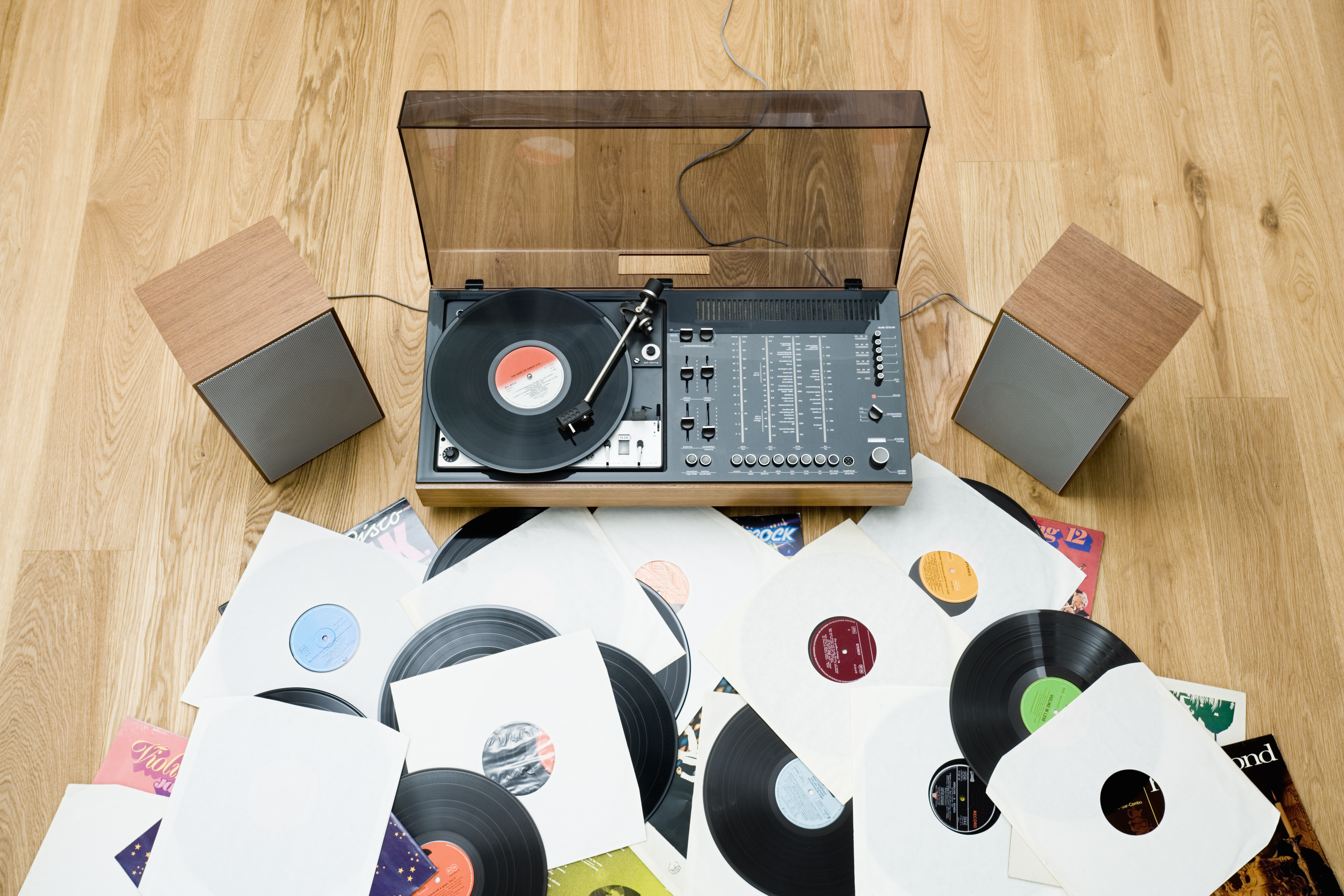 A record player with a record on the turntable, flanked by two speakers, with many records spilling out from under it.