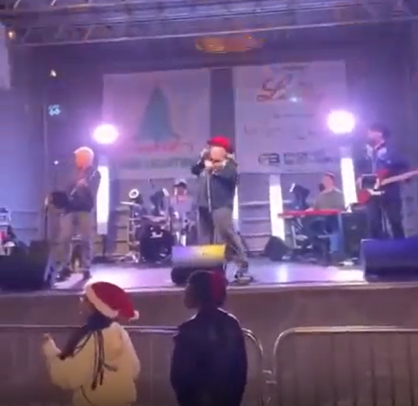 A band performing on stage with two children watching in front of barriers.