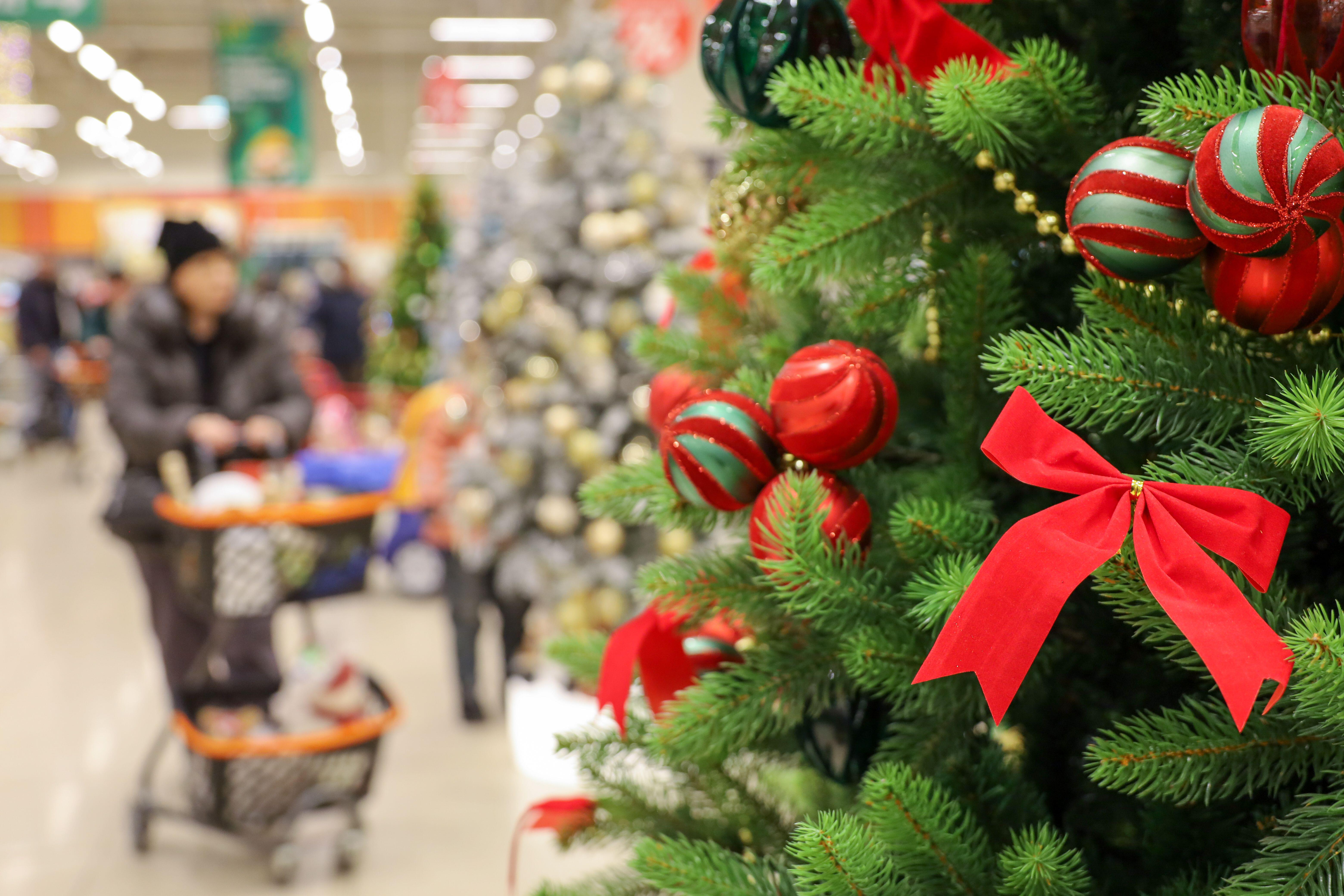 Christmas tree with red balls and ribbons in a shopping mall with people in the background.