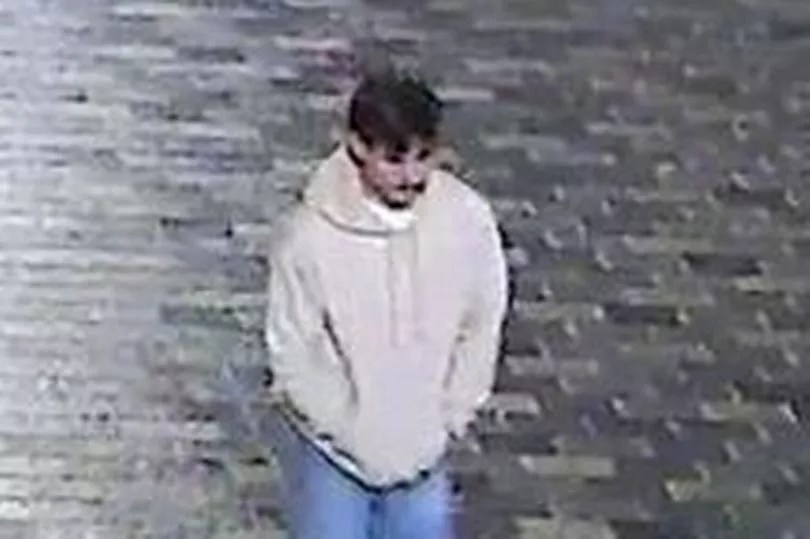 Surveillance footage of a man in a light-colored hoodie and blue jeans, seen from above.