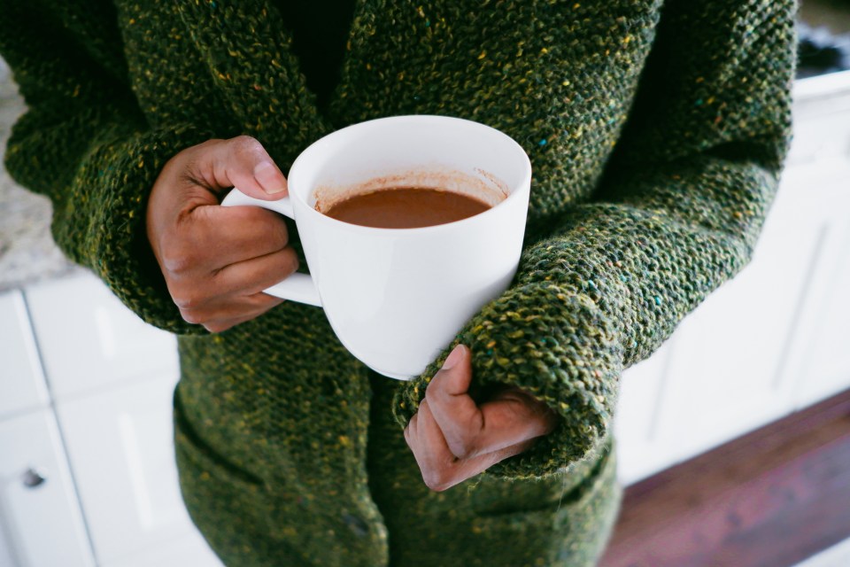 Woman holding a white mug of hot chocolate, wearing a green cardigan.
