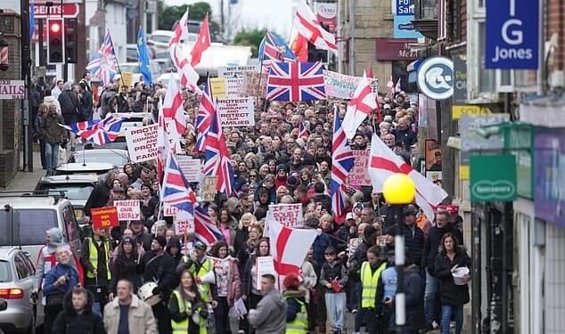 Protesters in Crowborough, East Sussex, hold placards and march through the town centre this morning over plans to house 600 male asylum seekers at Crowborough Training Camp