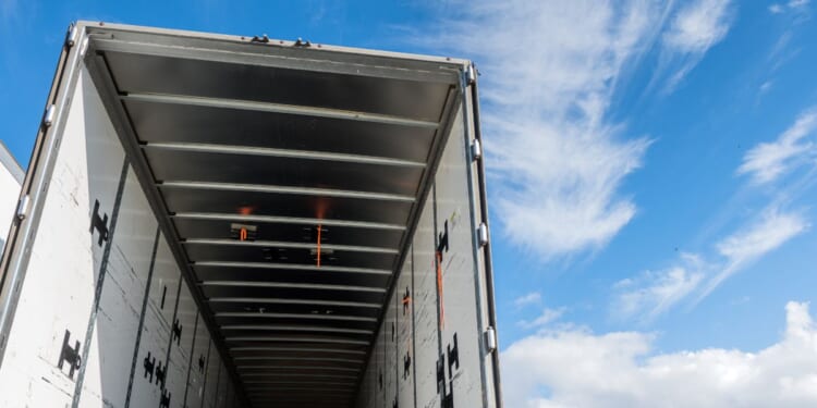 The view of the inside of the rear of a huge empty freight truck with the rear doors open.