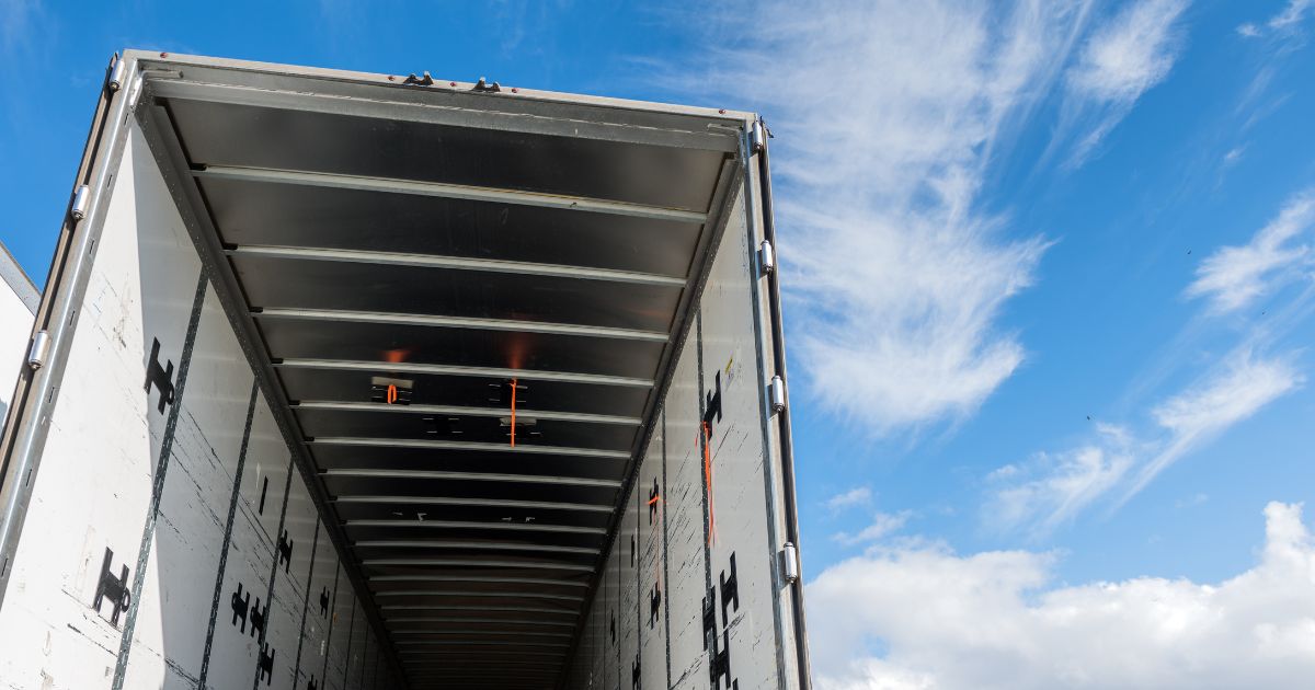 The view of the inside of the rear of a huge empty freight truck with the rear doors open.