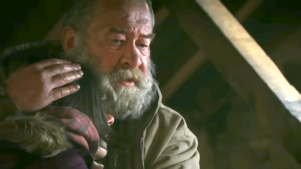 A man with a white beard is embracing a younger person, whose face is not fully visible.