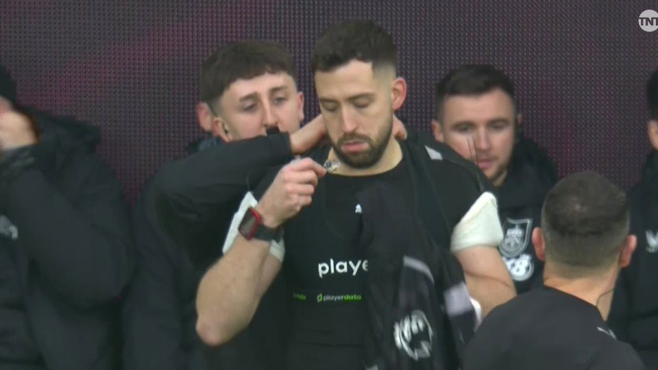 A male player being helped by another male to put on a GPS vest before a match.