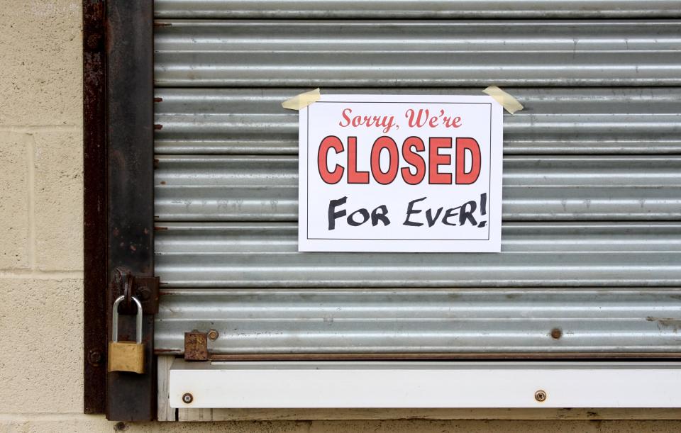 A sign reading "Sorry, We're CLOSED For Ever!" taped to a locked, corrugated metal business shutter.