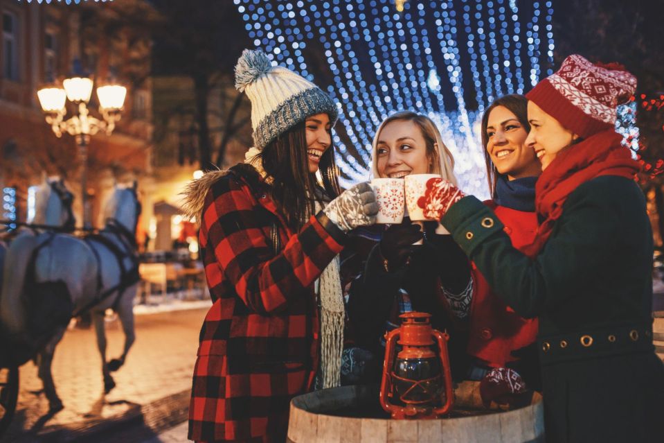An image collage containing 1 images, Image 1 shows Four friends in winter clothes cheer with mugs of mulled wine and hot tea on a street decorated with Christmas lights