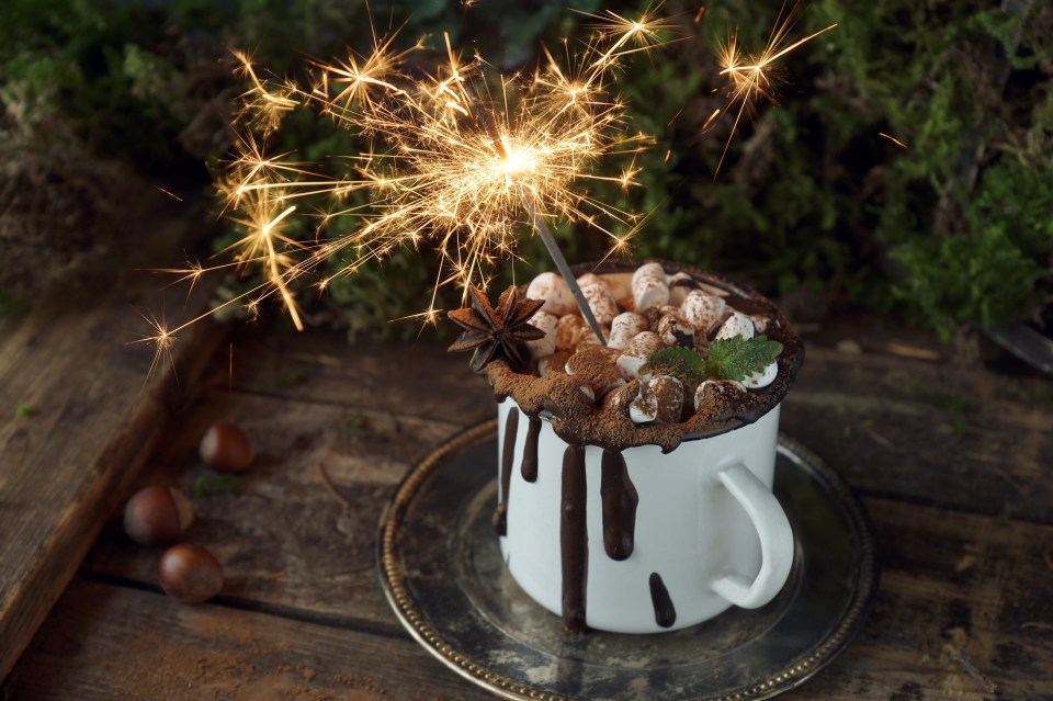 Hot chocolate in a mug topped with marshmallows, star anise, mint, and a lit sparkler.