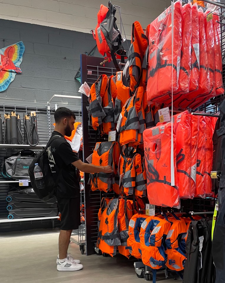 A man inspects life jackets in a store, while others hang on display.