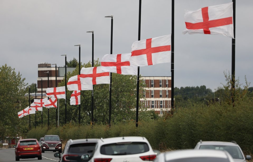 St. George's Cross flags flying from lampposts along a road with cars.